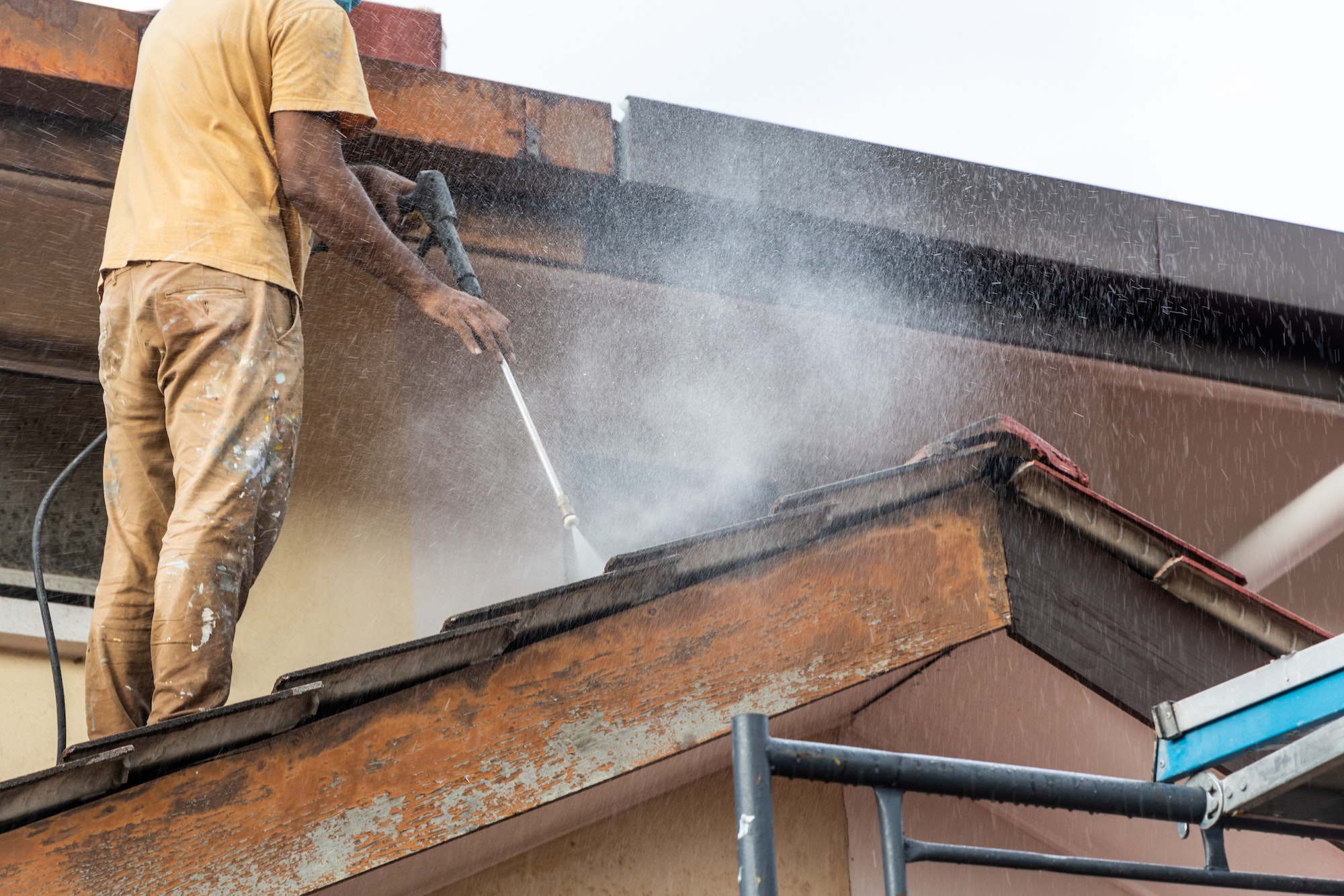 Worker using high pressure water jet spray gun to wash and clean dirt from rooftop tiles in